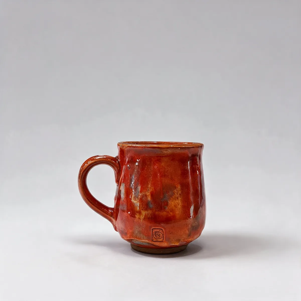Czerwony ceramiczny kubek na jasnoszarym tle.